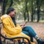 Young woman with yellow raincoat enjoying in the autumn park, using digital tablet